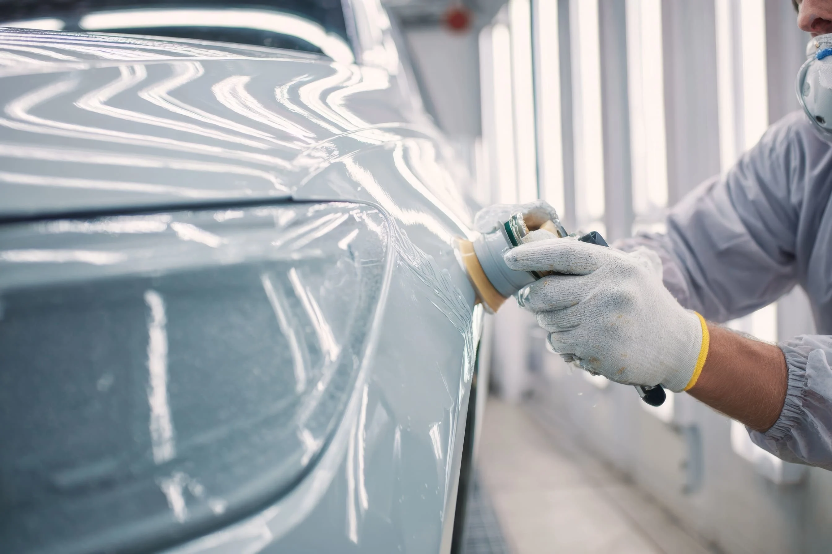 A worker wearing gloves uses a detailing tool on a car's surface, showcasing professional car detailing